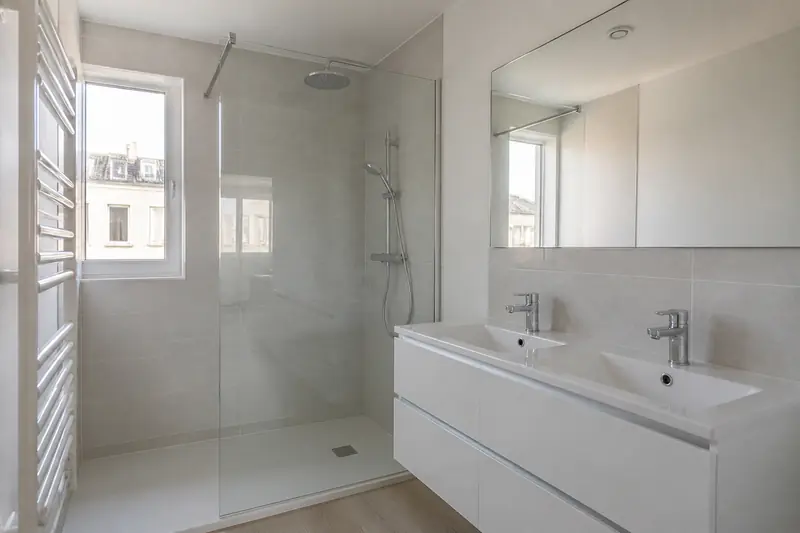 Salle de bain rénovée avec carrelage clair et douche à l'italienne